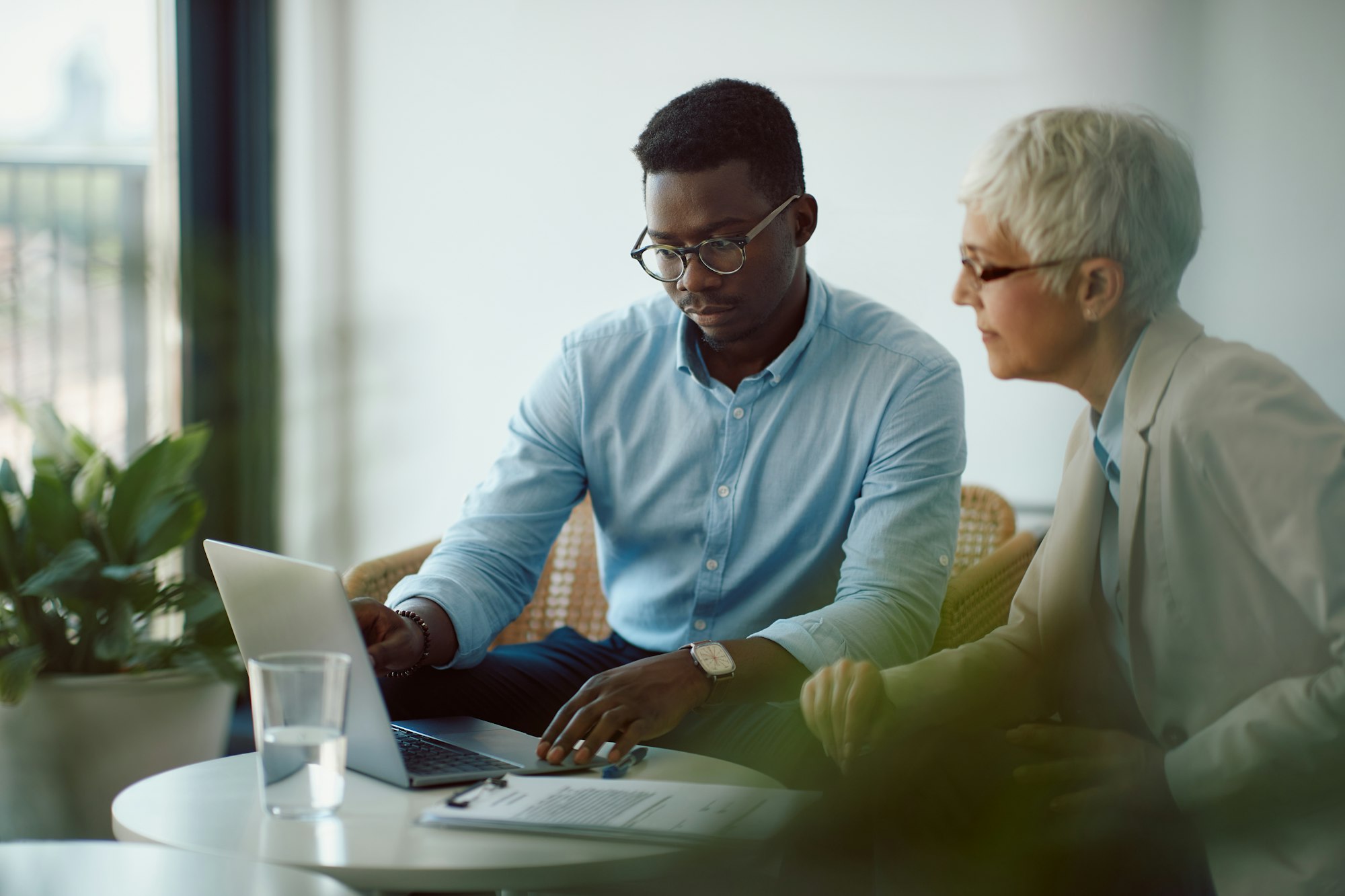 Black businessman and his mature colleague using laptop while working in the office.